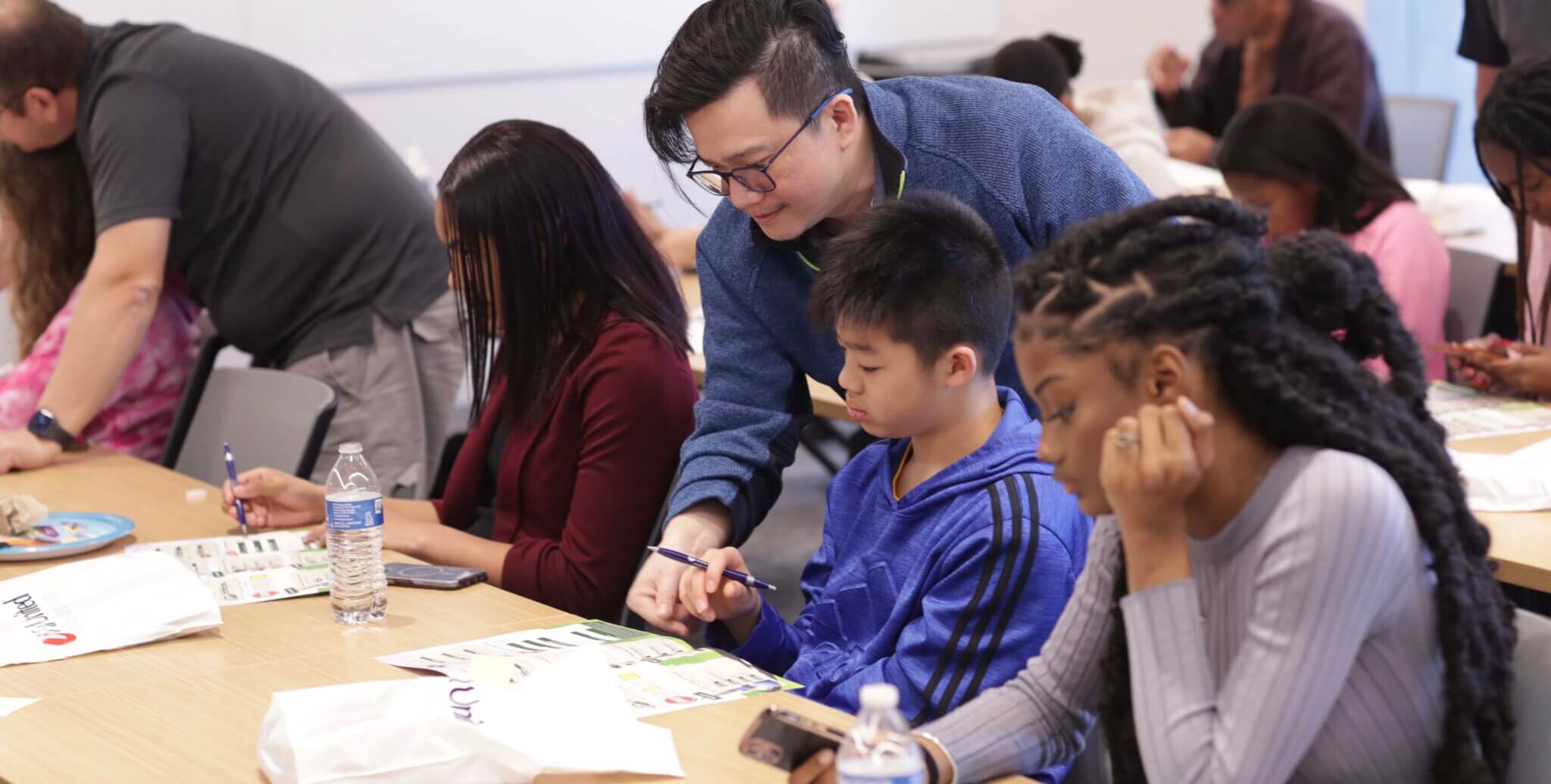 Teacher guiding student in collaborative classroom workshop with diverse participants learning together.