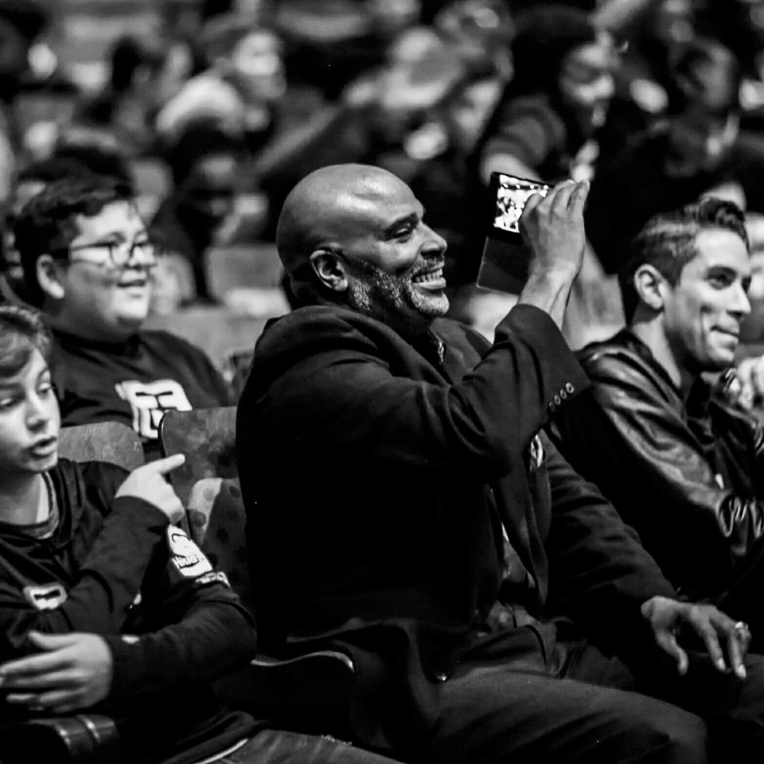 Top Achievers Founder Lawrence Mann and an excited crowd enjoying indoor Esports gaming event in black and white.