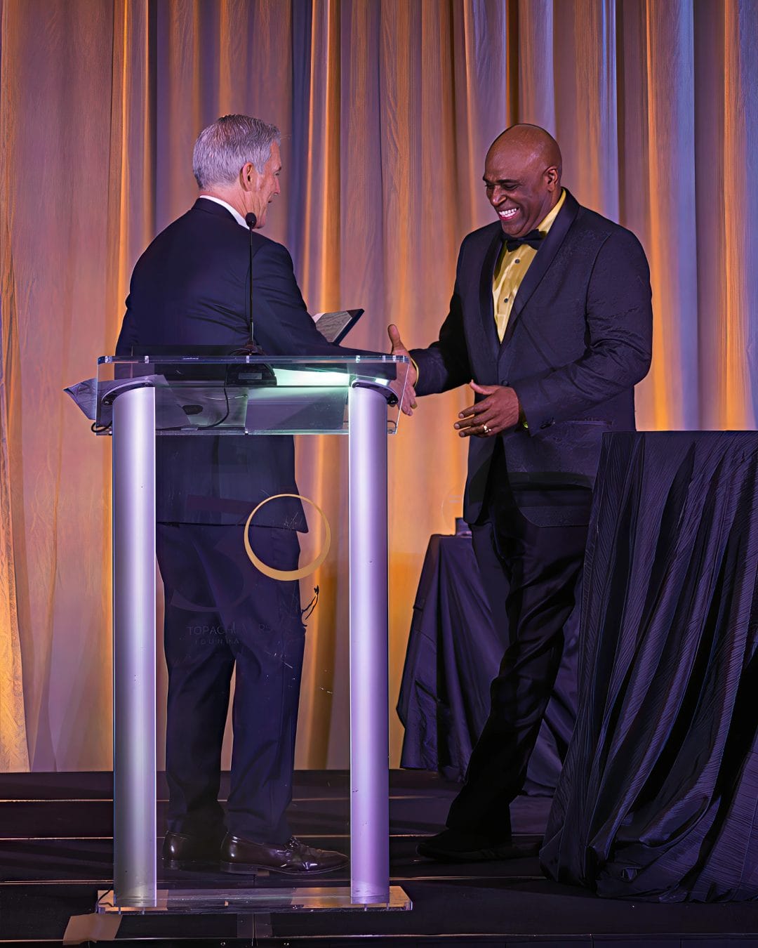 City of Plano Honors Lawrence Mann with Key to the City and Declares May 1, 2026, "Lawrence Mann Day" 2 Lawrence Mann shakes hands with Plano Mayor John Muns at the Top Achievers Foundation 30th Anniversary Gala podium.